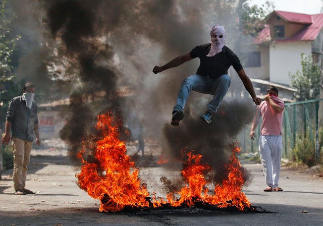 A man in a balaclava jumps over burning debris during a protest against the recent killings in Kashmir, in Srinagar, India September 12, 2016. PHOTO: REUTERS