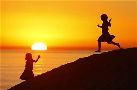 The sun sets under smoky skies as girls play in the sand. PHOTO: REUTERS