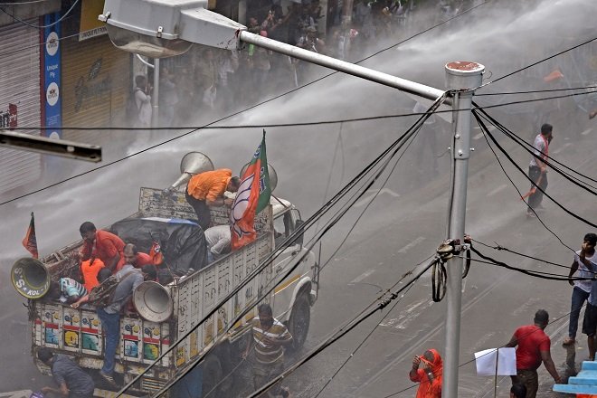 BJP activists shelter on the back of a truck as police use a water canon to disperse demonstrators. PHOTO: AFP