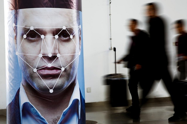 FILE PHOTO:People walk past a poster simulating facial recognition software at the Security China 2018 exhibition on public safety and security in Beijing, China October 24, 2018. PHOTO: REUTERS