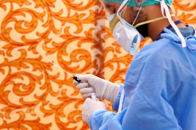 A health worker wearing protective gears, holds a nose-swab, collected at the walk-through screening and testing facility for the coronavirus disease (COVID-19), in Karachi. PHOTO: REUTERS