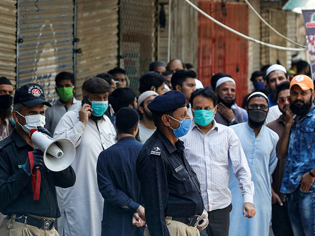 A police officer uses a megaphone to disperse shopkeepers gathered to reopen their shops at a closed market in Karachi. PHOTO: REUTERS/FILE