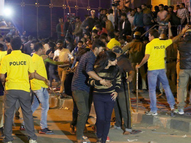 An Indian man helps a woman (C) leave as police personnel try to manage crowds during New Year's Eve celebrations in Bangalore on January 1, 2017. PHOTO: AFP