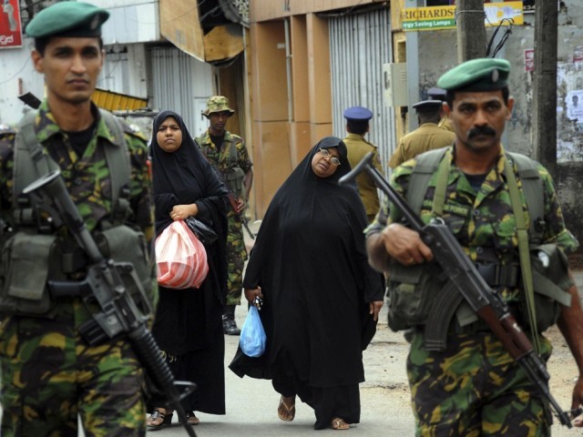 Two Muslim women walk behind patrolling Special Task Force Commandos outside the mosque that was vandalised. PHOTO: REUTERS