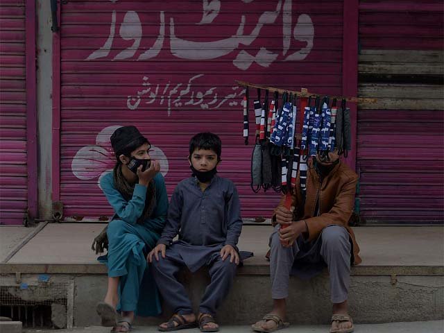 Children selling face masks wait for customers at a closed market area in Rawalpindi. PHOTO: AFP