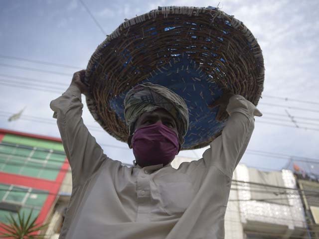 A labourer wearing a face mask carries his basket as he searches for customers. PHOTO: AFP